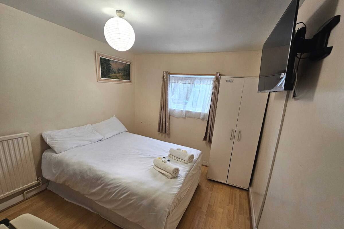 Un dormitorio con cama, radiador, armario, televisor y ventana con cortinas.