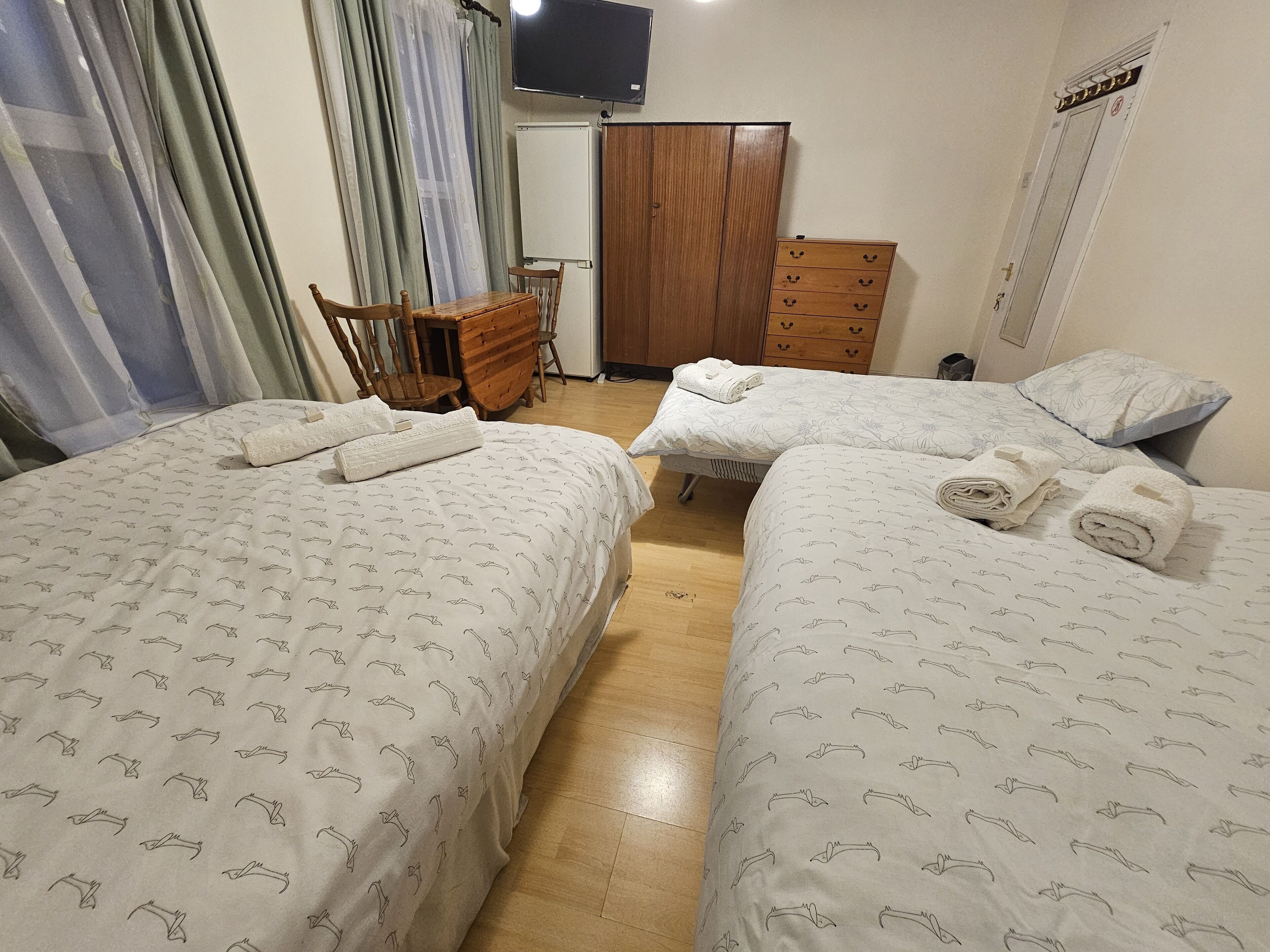 Ein Hotelzimmer mit zwei Betten, einem Holzschrank, einem Schreibtisch mit Stuhl und einem an der Wand befestigten Fernseher.