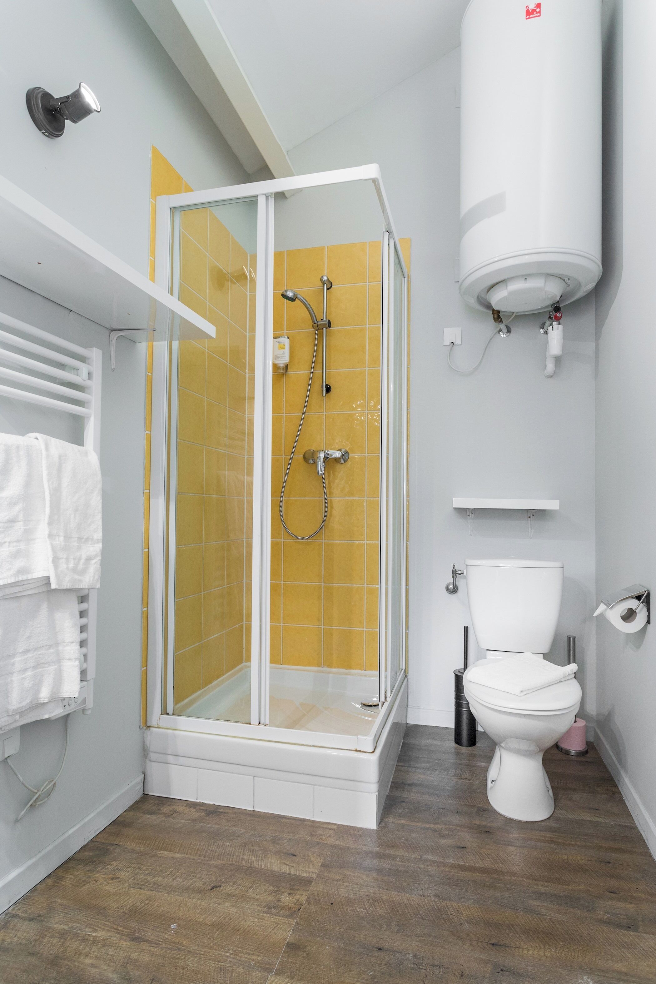 Un baño con ducha envuelta en vidrio, un inodoro blanco y una pared de azulejos amarillos.