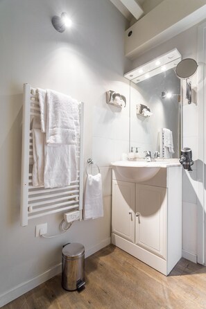 Un baño con lavamanos blanco, espejo y toallero.