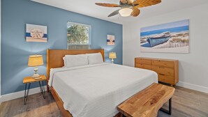 Ein Schlafzimmer mit einem Bett, Nachttischen, einer hölzernen Bank, einem Deckenventilator und Kunstwerken an den Wänden.