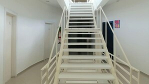 Una escalera blanca con barandilla que lleva a un rellano con una lámpara en el techo.