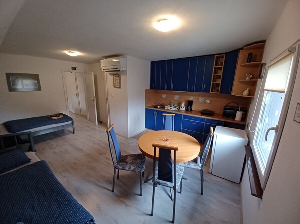 A compact kitchen with blue cabinets, a wooden dining table, and a bench.