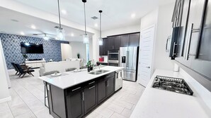 Uma cozinha moderna com ilha central, armários escuros, eletrodomésticos de aço inoxidável e iluminação pendente.