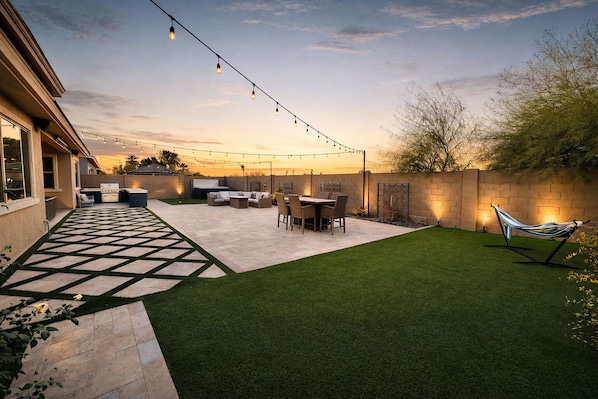 A backyard with artificial grass, a barbecue area, outdoor furniture, and string lights.