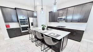 Uma cozinha moderna com armários escuros, eletrodomésticos de aço inoxidável, uma ilha central com banquetas e iluminação pendente.