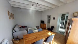 A modern living room with a wooden dining table, blue chairs, a grey sofa, and a television. - La Maisonnette du Marais - 1 à 6 Pers (Doix lès Fontaines)