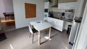 A modern kitchen with white cabinets, a dining table with chairs, and a black trash bin. - La Maisonnette du Marais - 1 à 6 Pers (Doix lès Fontaines)