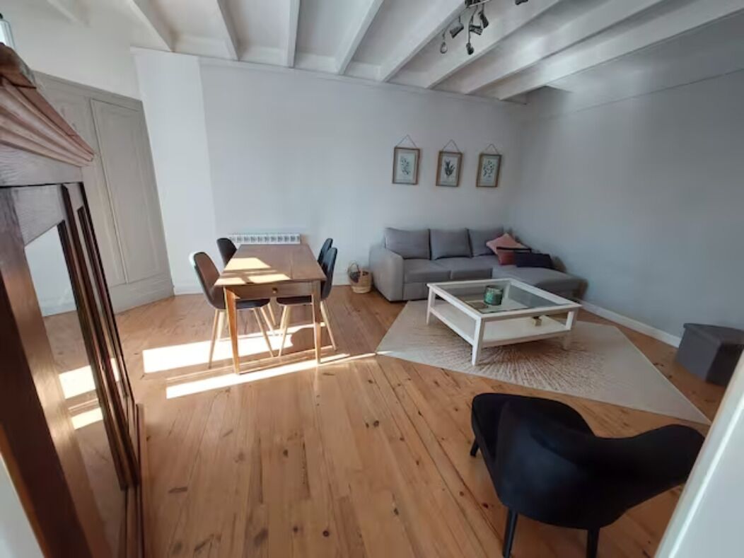Una sala de estar moderna con piso de madera, un sofá gris, una mesa de centro blanca y una mesa de comedor con sillas.