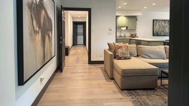 A modern living room with a sectional sofa, a large abstract painting, and a kitchen in the background. - Recently remodeled 3bdr condo in Lionshead (Vail)