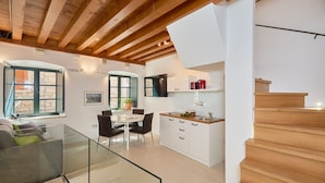 Een moderne keuken met witte kasten, een houten trap en een eethoek met een glazen tafel en stoelen.