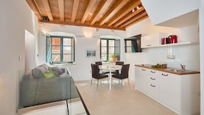Een moderne keuken met witte kastjes, een houten plafond en een eethoek met een glazen tafel en stoelen.