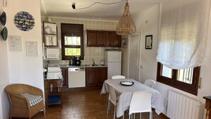 Et kompakt køkken med spiseplads, med et spisebord med stole, en fletstol og en indbygget ovn.