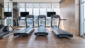 A modern gym with treadmills, a stationary bike, and a rowing machine. Large windows offer a city view.