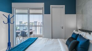 A hotel room with a large bed, a balcony with a table and chairs, and a city view.