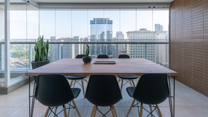 A modern conference room with a large table and six chairs, large windows with a city view, and potted plants.