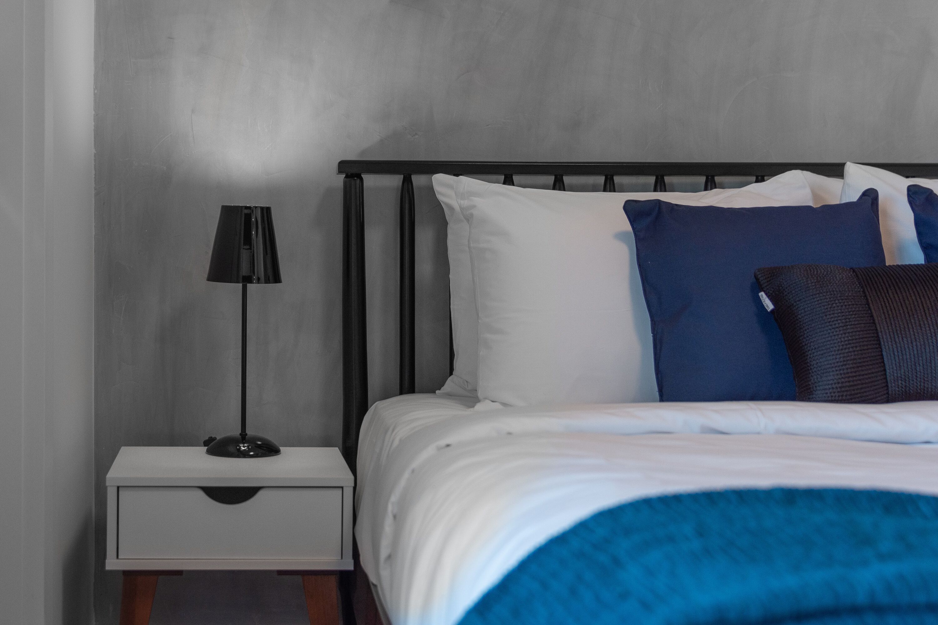 A neatly made bed with white and blue bedding, a black metal headboard, and a bedside table with a lamp.