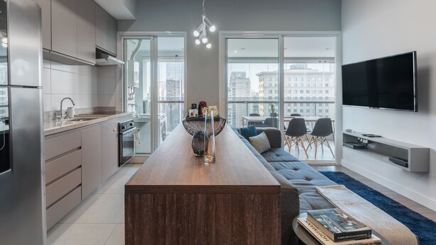 A modern kitchen with a central island, a dining area with a sofa, and a large TV on the wall.