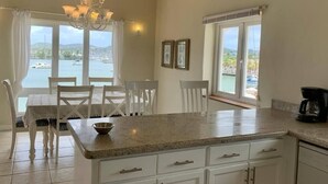 Una cocina con una isla grande, armarios blancos y vista al mar.