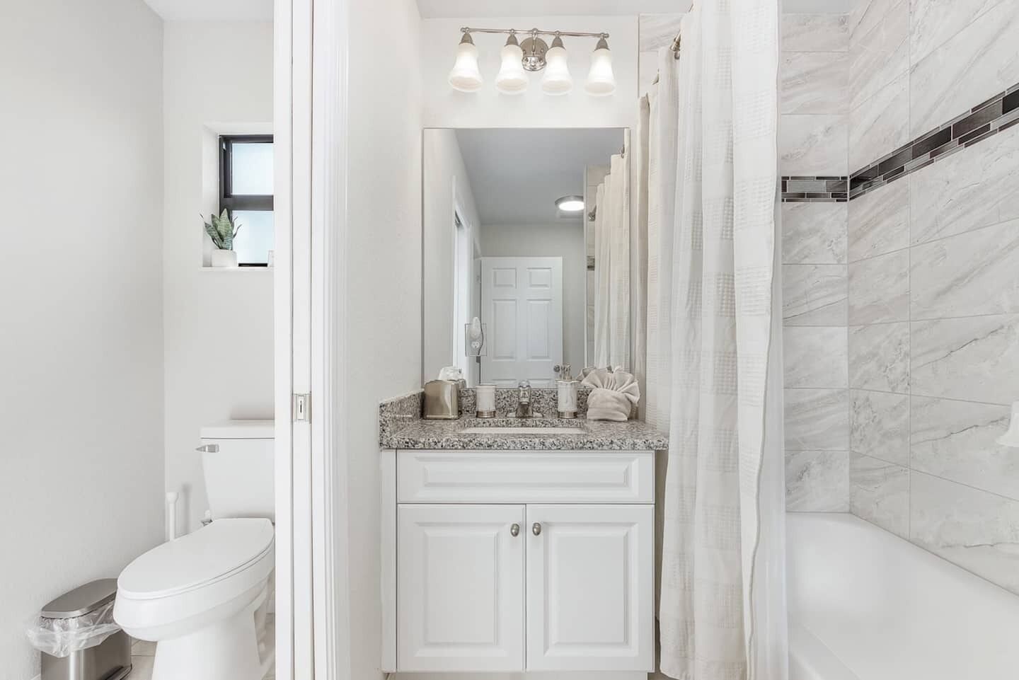 Une salle de bain moderne avec des toilettes blanches, un lavabo sur un plan de travail en granit et un espace douche avec un mur carrelé.