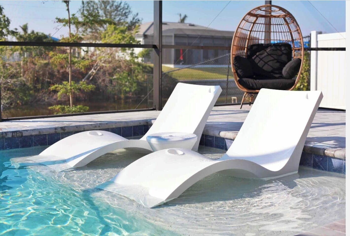 Une piscine avec trois chaises longues blanches et un fauteuil en osier.