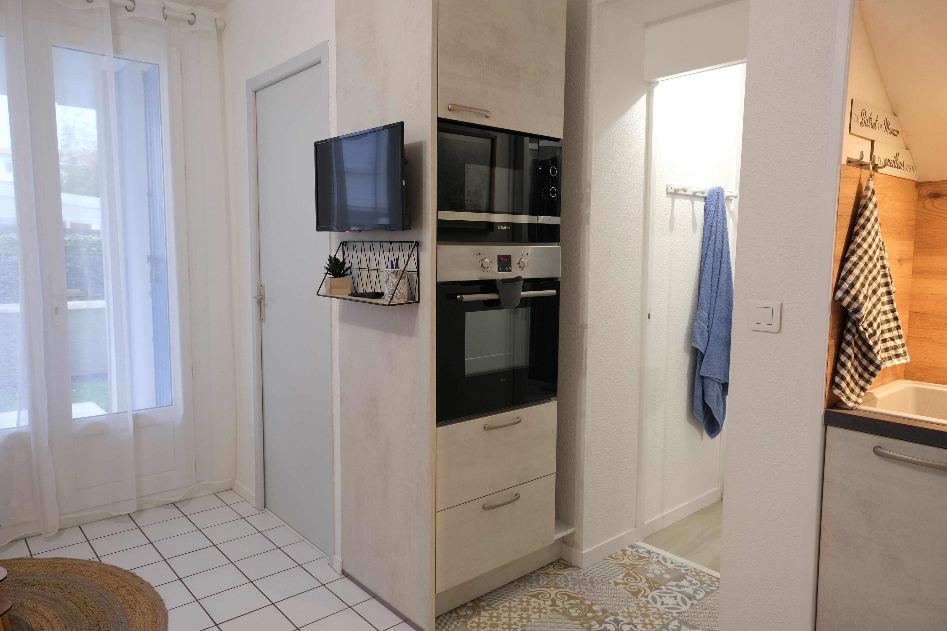 Une cuisine compacte équipée d’un four encastré, d’un micro-ondes et d’un téléviseur fixé au mur.