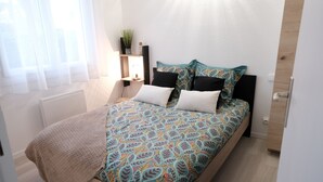 A neatly made bed with patterned bedding, a bedside table with a lamp, and a small plant on the wall. - T2 apartment with garden and parking, ROYAN, near seafront (Royan)