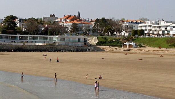 A sandy beach with people walking and playing, buildings in the background, and a clear sky. - T2 apartment with garden and parking, ROYAN, near seafront (Royan)