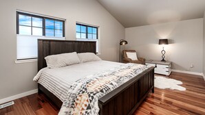 A bedroom with a large bed, two windows, a ceiling fan, a chair, a nightstand, and a lamp. - Cowboy Cabin on Cooper (Red Lodge)