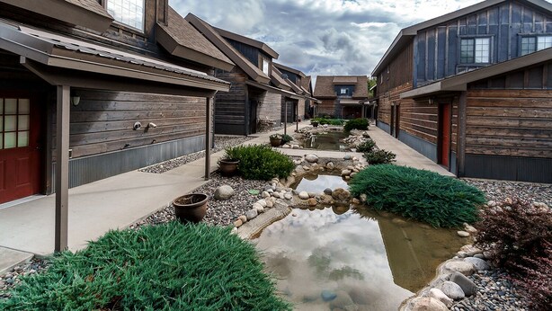 A modern residential complex with a central water feature, wooden exterior walls, and a clear sky. - Cowboy Cabin on Cooper (Red Lodge)