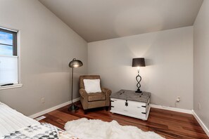 A bedroom with a sloped ceiling, a brown chair with a white pillow, a floor lamp, a dresser with a lamp, and a white fluffy rug. - Cowboy Cabin on Cooper (Red Lodge)