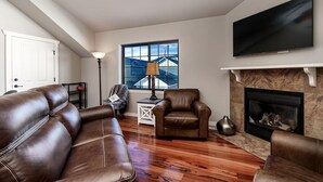 A living room with leather sofas, a fireplace, a television, and a window with a view of a building. - Cowboy Cabin on Cooper (Red Lodge)