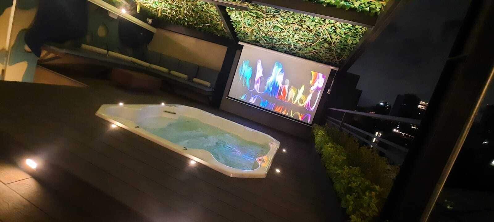 Un bain à remous doté d’un écran numérique affichant des graphiques colorés, entouré d’un espace de détente extérieur moderne avec un mur végétal et un escalier.