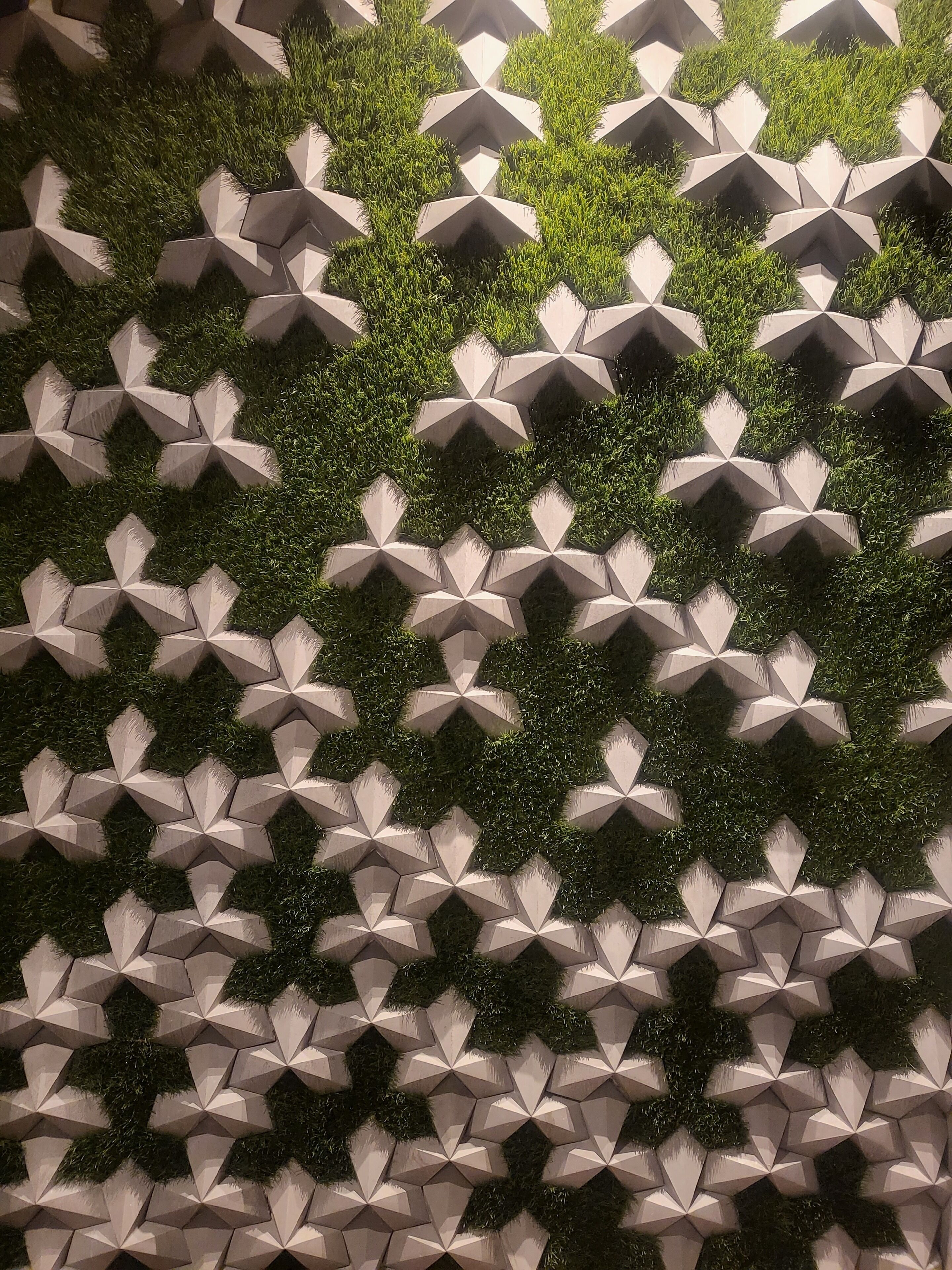 Pared con diseño geométrico y jardineras empotradas con plantas verdes.