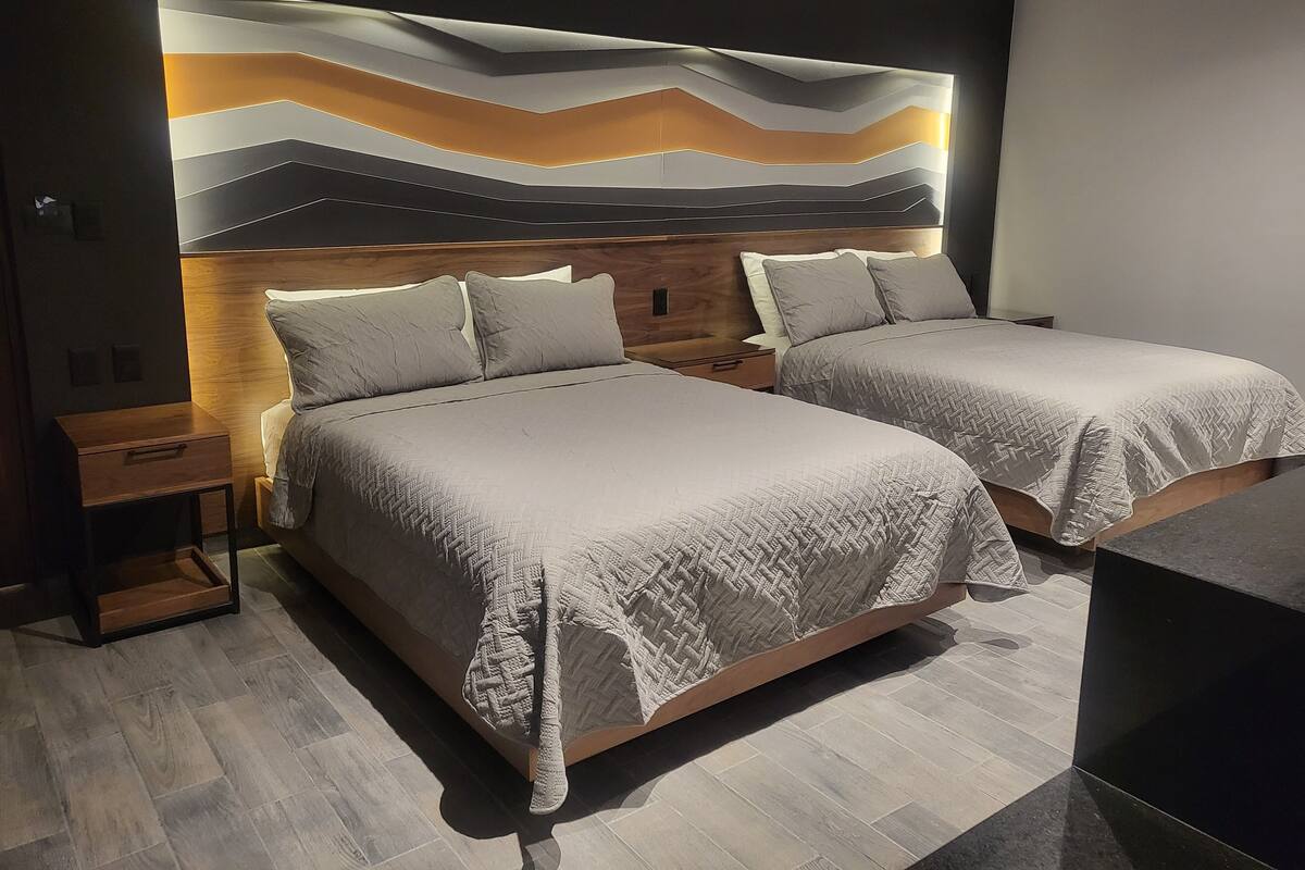 A modern hotel room with two beds, a wooden headboard, and a large abstract wall art piece.