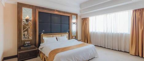 A hotel room with a large bed, a nightstand, a mirror, and a window with curtains.