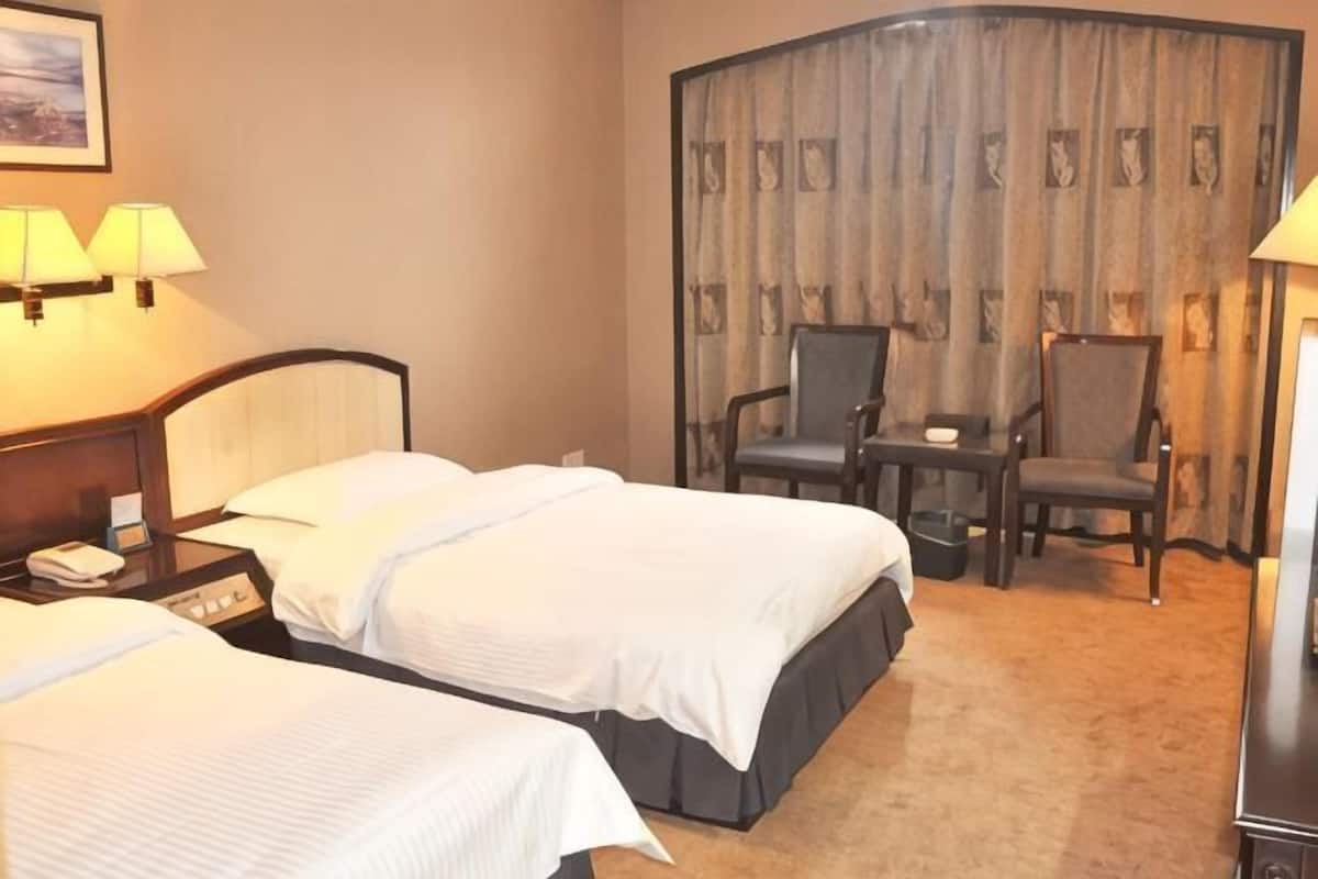 A hotel room with two beds, a desk, a chair, and a curtain.