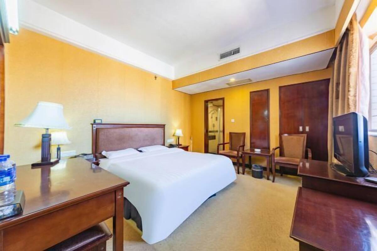 A hotel room with a bed, desk, chair, TV, and lamp.