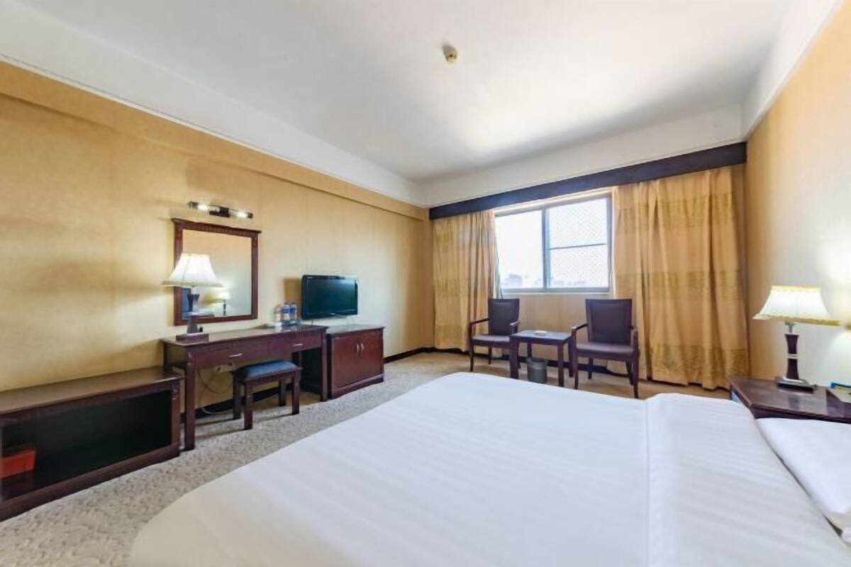 A hotel room with a large bed, a desk with a television, a chair, and a window with curtains.