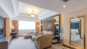 A spacious hotel room with a large bed, a seating area with a sofa and armchairs, a desk with a chair, and a large mirror. - Tianma Hotel (Shantou)