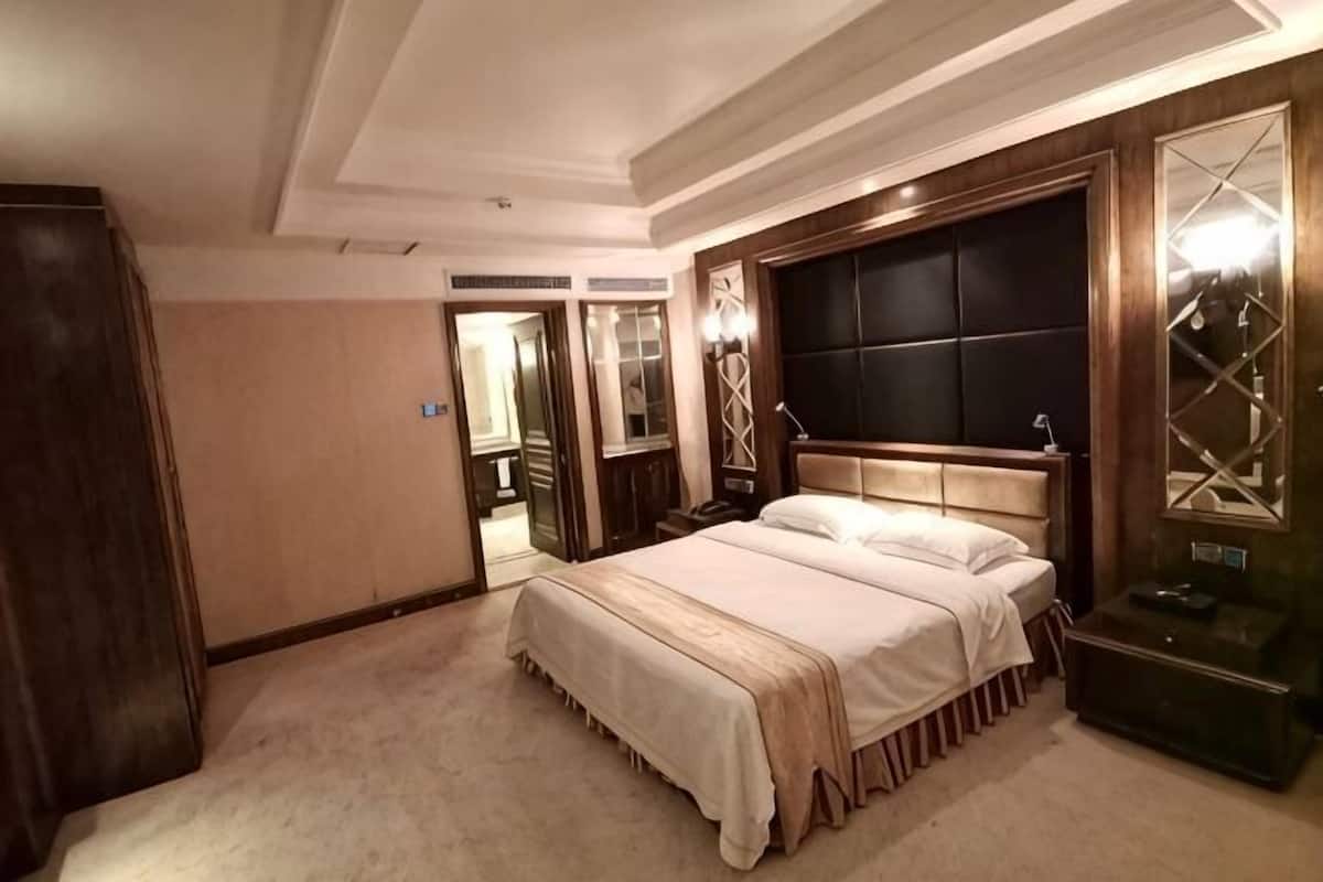 A hotel room with a large bed, a wooden headboard, a mirror, and a wardrobe.