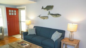 A living room with a blue sofa, two side tables with lamps, a wooden coffee table, and three whale wall art pieces.