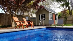 A swimming pool with a wooden deck and two orange chairs.