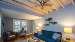 A cozy living room with a blue sofa, two wicker chairs, a wooden coffee table, and a ceiling fan.