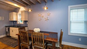A dining area with a wooden table and chairs, a kitchen with white cabinets, and a blue wall with star decorations.