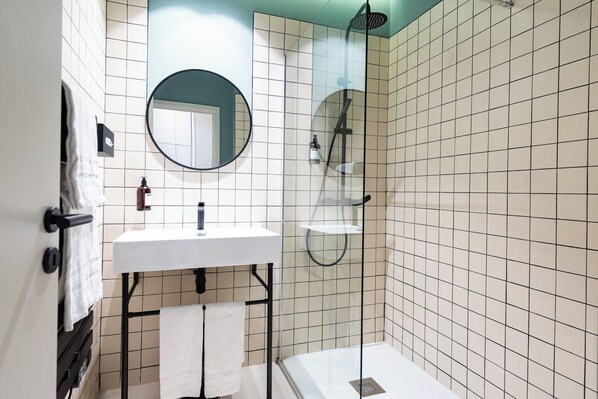 A modern bathroom with a white sink, a round mirror, a handheld showerhead, and a glass-enclosed shower.