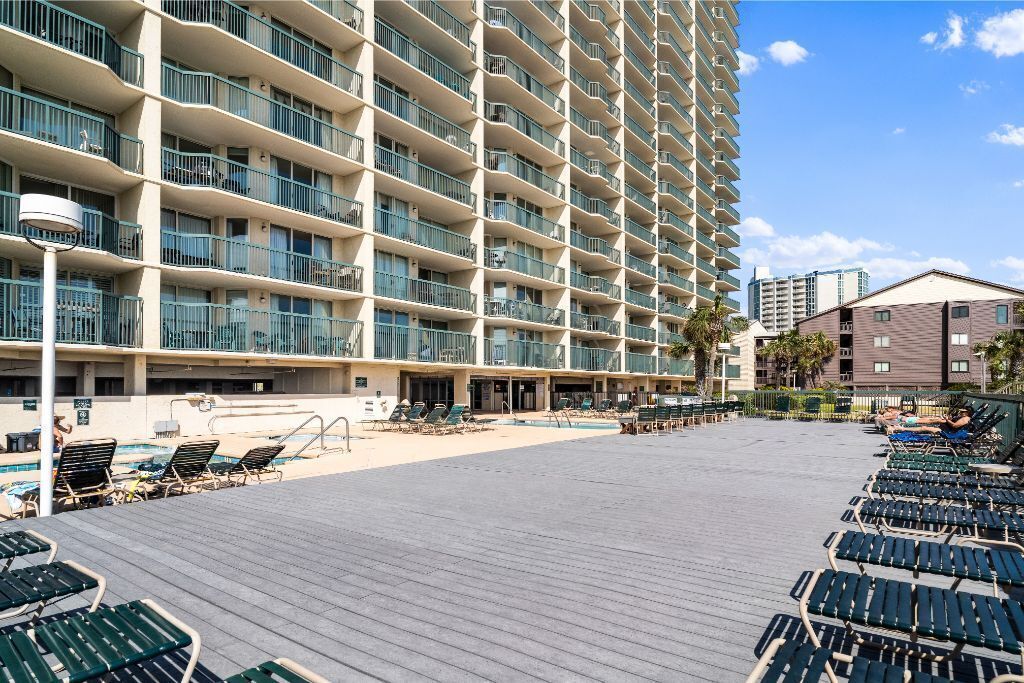 A hotel with multiple balconies, a pool area with sun loungers, and a beachside view.