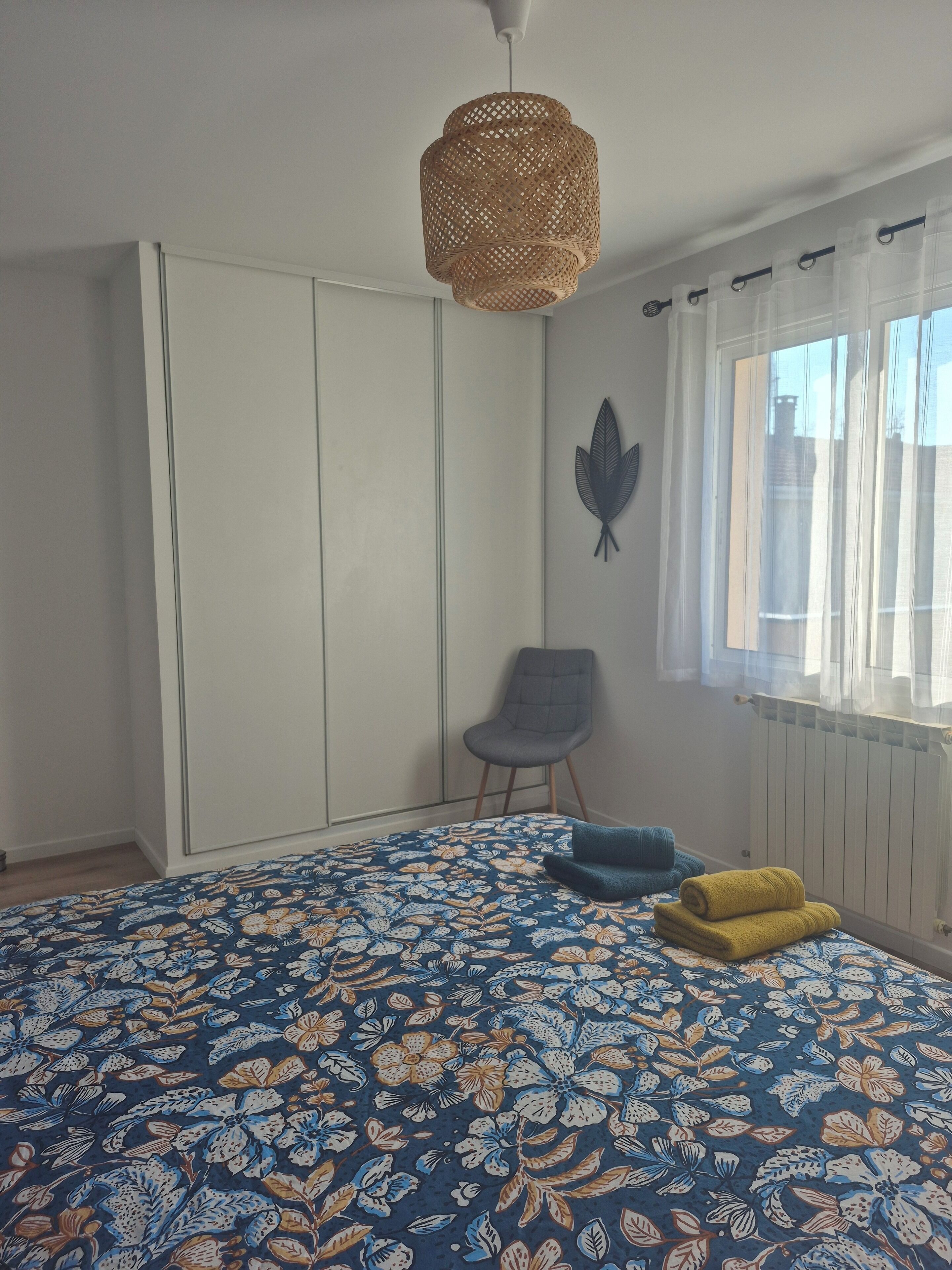 A bedroom with a bed, a chair, a wardrobe, a radiator, and a window with curtains.