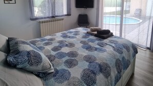 Ein Schlafzimmer mit Bett, Fernseher, Fenster und Blick auf einen Pool.