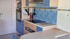 Eine kleine Küche mit blauen Schränken, einer Edelstahl-Dunstabzugshaube und einem runden Esstisch mit blauen Stühlen.